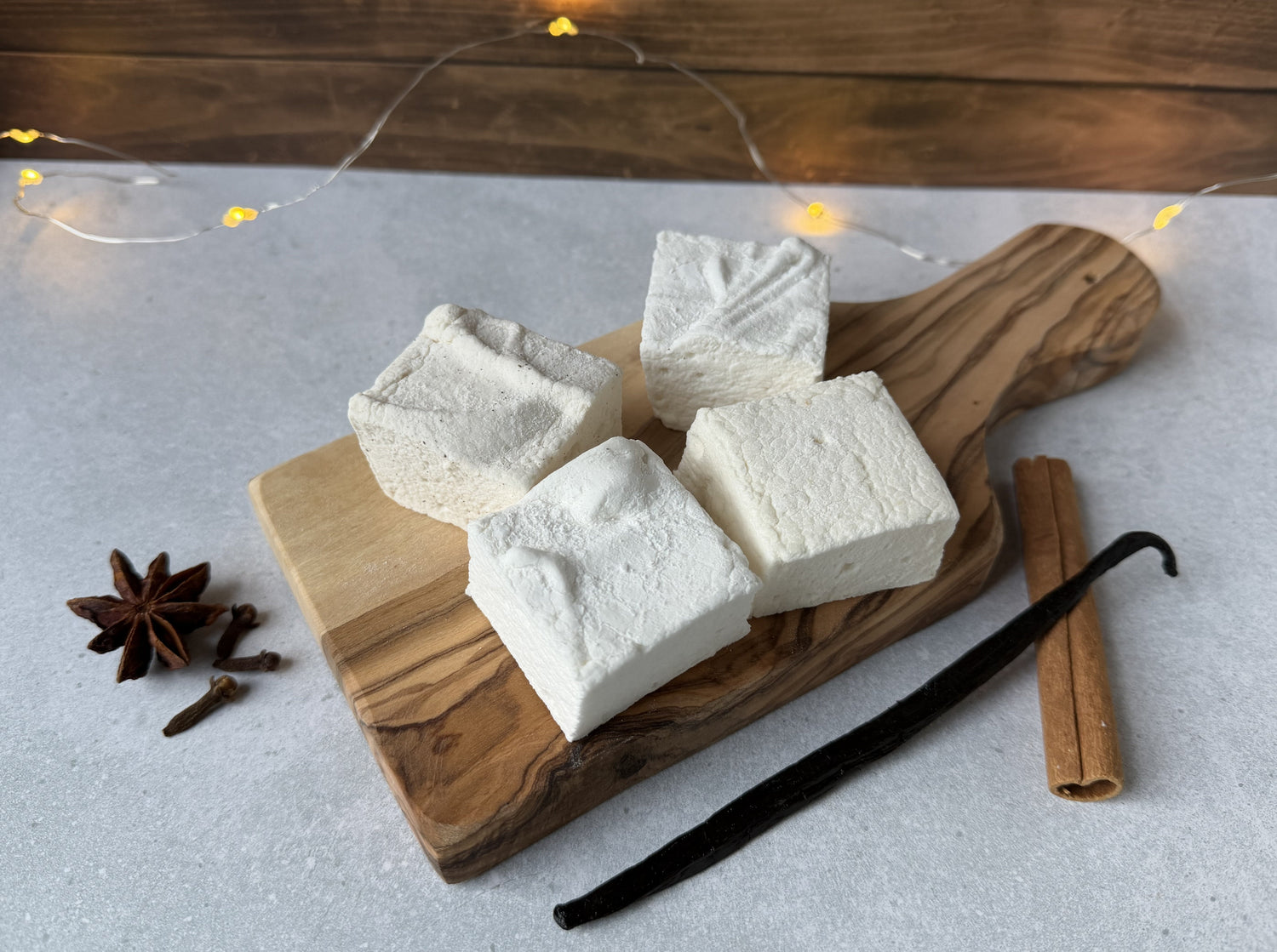 Handcrafted cozy marshmallow flavors, including cinnamon, chai, vanilla, and butterscotch, arranged on olive wood serving boards with warm spices.