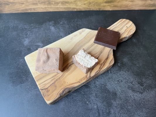 Handcrafted chocolate marshmallows dusted with cocoa on an olive wood board