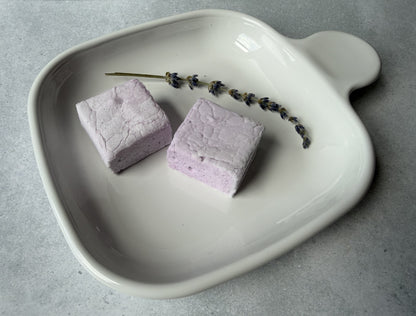 Handcrafted Lavender marshmallows on a white ceramic plate with a sprig of dried lavender. Two marshmallows showcase their soft lavender color and fluffy handcrafted texture.